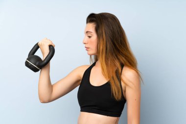 Genç esmer kız halter kaldırıyor. Arka planda kettlebell var.