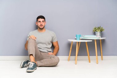 Genç yakışıklı adam yerde oturuyor ve yan tarafa bakıyor.