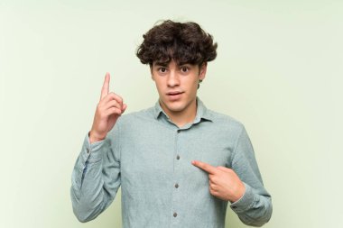 Sürpriz yüz ifadesi ile izole yeşil duvar üzerinde genç adam