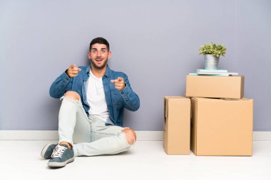 Yakışıklı genç adam kutuları arasında yeni bir evde hareket size parmak işaret