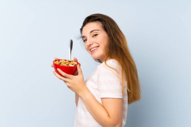 Genç esmer kız arka planda bir kase mısır gevreği tutuyor.