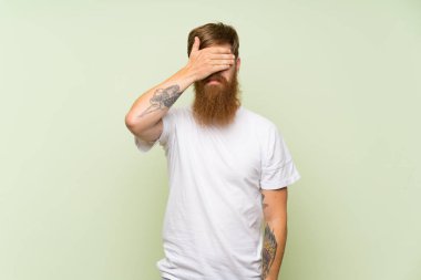 Kızıl saçlı, uzun sakallı, yeşil arka planda, gözleri elleriyle kaplayan bir adam. Bir şey görmek istemiyorum.