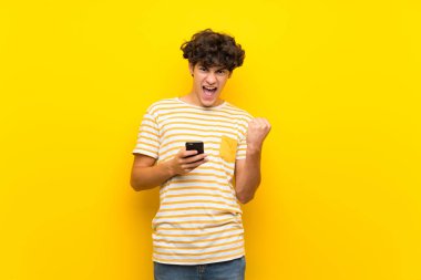 Zafer pozisyonunda telefon ile izole sarı duvar üzerinde genç adam