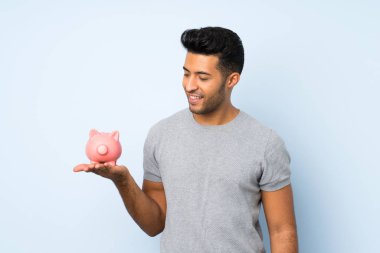 Büyük bir kumbara tutan izole arka plan üzerinde genç yakışıklı adam