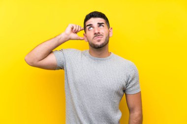 Soyutlanmış sarı arka planda genç yakışıklı bir adam. Şüpheleri var ve kafası karışık.