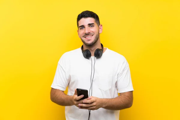 Νέος όμορφος άνδρας ακούγοντας μουσική με ένα κινητό πάνω από απομονωμένο κίτρινο τοίχο — Φωτογραφία Αρχείου