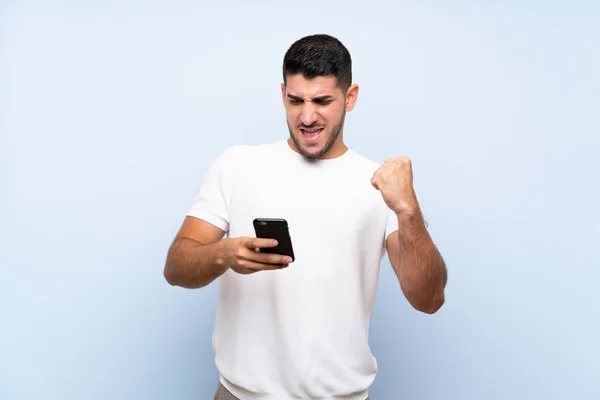 Kaukasischer Gutaussehender Mann Vor Isoliertem Blauem Hintergrund Mit Telefon Siegerposition — Stockfoto