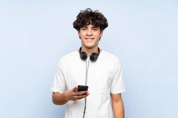 Joven Escuchando Música Con Móvil Sobre Una Pared Azul Aislada —  Fotos de Stock