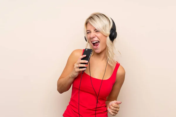 Νεαρή Ξανθιά Γυναίκα Απομονωμένο Φόντο Χρησιμοποιώντας Κινητό Ακουστικά Και Τραγούδι — Φωτογραφία Αρχείου