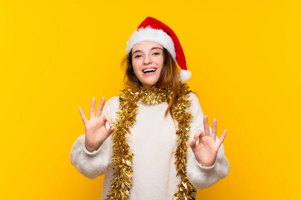 在孤立的黄色背景上戴着圣诞帽的女孩 手指头上有个好的标志 — 图库照片