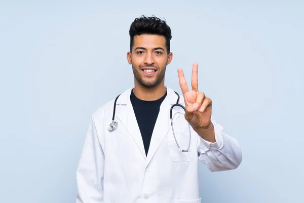 Młody Lekarz Człowiek Białym Tle Niebieską Ścianę Uśmiechnięty Pokazując Znak — Zdjęcie stockowe