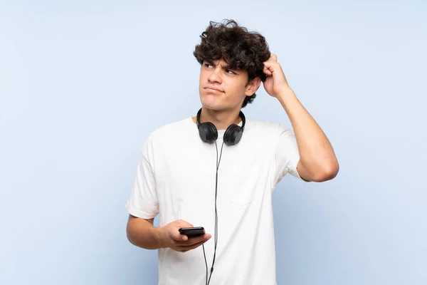 Joven Escuchando Música Con Móvil Sobre Una Pared Azul Aislada —  Fotos de Stock