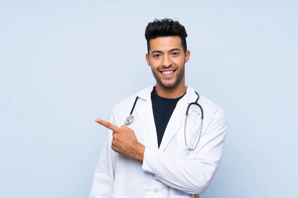 Joven Médico Sobre Una Pared Azul Aislada Apuntando Hacia Lado —  Fotos de Stock