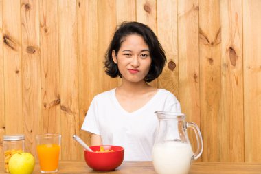 Asyalı genç kadın şüpheler ve kafa karıştırıcı yüz ifadesi ile kahvaltı süt sahip