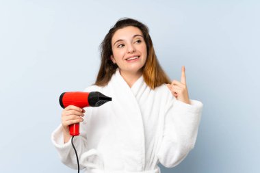 Saç kurutma makinesiyle bornozlu genç bir kadın parmağını kaldırarak çözümü bulmaya çalışıyor.