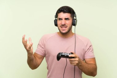 İzole yeşil duvar üzerinde bir video oyunu denetleyicisi ile oynayan genç yakışıklı adam