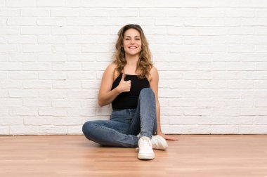 Genç sarışın kadın jest kadar bir başparmak vererek katta oturan