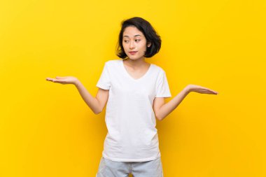 İki eliyle copyspace tutan izole sarı duvar üzerinde Asyalı genç kadın