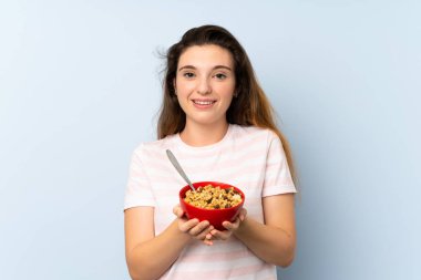 Genç esmer kız arka planda bir kase mısır gevreği tutuyor.