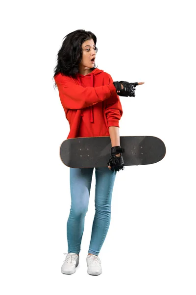 孤立した白い背景の上に驚きと指摘側の若いスケーターの女性の完全長ショット — ストック写真