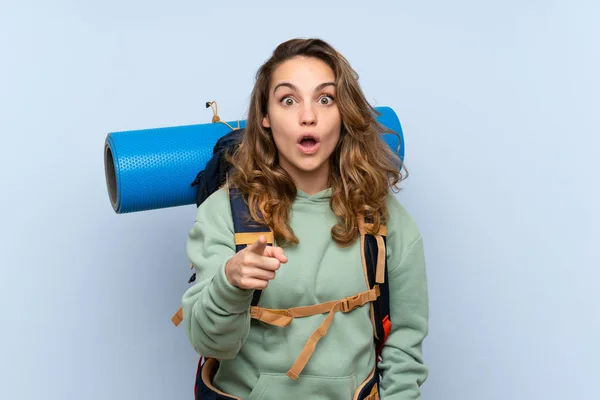 Jovem Loira Caminhante Menina Sobre Isolado Fundo Azul Surpreso Apontando — Fotografia de Stock