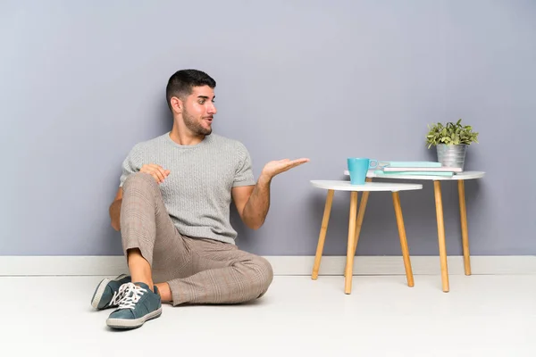 Jovem Homem Bonito Sentado Chão Segurando Copyspace Imaginário Palma Mão — Fotografia de Stock