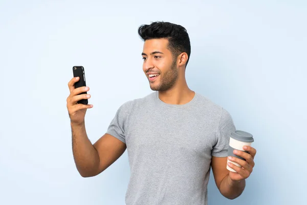 年轻的帅哥在孤立的背景拿着咖啡带走和手机 — 图库照片