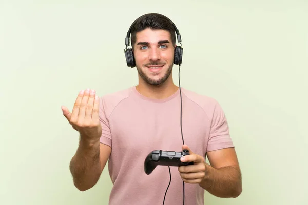 Молодой Красивый Мужчина Играет Контроллером Видеоигры Над Изолированной Зеленой Стеной — стоковое фото
