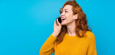 Sarı kazaklı kızıl saçlı kadın cep telefonuyla sohbet ediyor.
