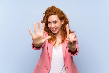 Kırmızı elbiseli kadın mavi duvarın üstünde altı parmaklı sayıyor.