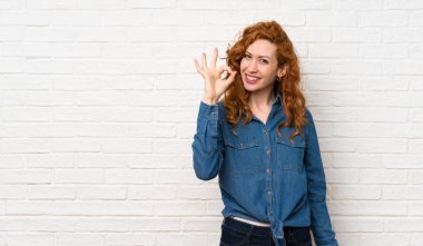 Beyaz tuğla duvarın üzerinde kızıl saçlı kadın parmaklarıyla işaret veriyor.