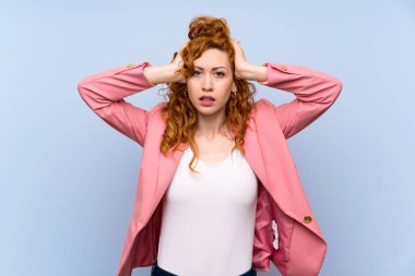 Kızıl saçlı kadın mavi duvarın üstünde hayal kırıklığına uğramış ve ellerini başının üstüne koyuyor.