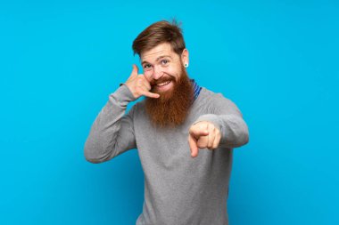 Kızıl saçlı, uzun sakallı, mavi arka planlı, telefon hareketleriyle ön tarafı işaret eden bir adam.