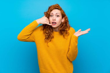 Sarı kazaklı, kızıl saçlı bir kadın telefon jesti yapıyor.