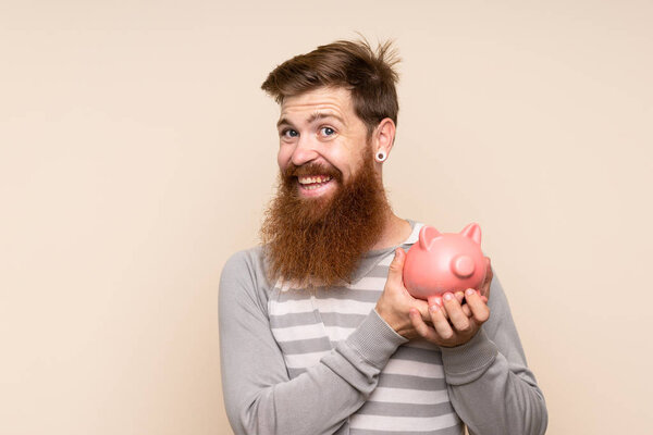 Redhead man with long beard over isolated background holding a big piggybank