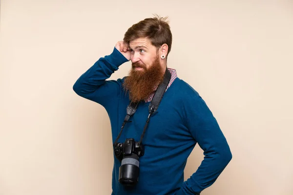 Redhead man with long beard over isolated background with a professional camera and thinking