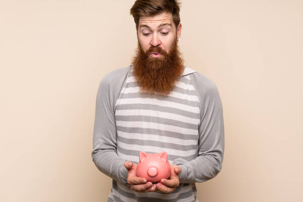 Redhead man with long beard over isolated background holding a big piggybank