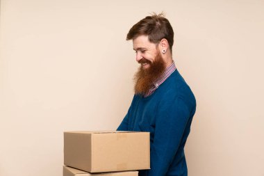 Kızıl saçlı, uzun sakallı, izole bir geçmişi olan bir adam başka bir yere taşımak için bir kutu tutuyor.