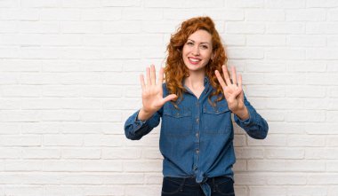 Beyaz tuğlalı duvarın üzerindeki kızıl saçlı kadın parmaklarıyla dokuzu sayıyor.