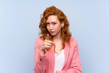 Kırmızı elbiseli kadın mavi duvarın üstünde hayal kırıklığına uğramış ve ön tarafı işaret ediyor.