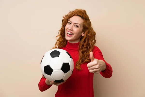 Redhead woman with turtleneck sweater holding a soccer ball