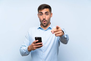 Cep telefonuyla genç yakışıklı adam mavi duvarı aşmış şaşırmış ve ön tarafı göstermiş.