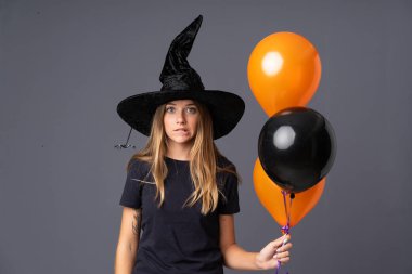 Siyah ve turuncu hava balonları tutan genç cadının şüpheleri ve kafa karıştırıcı bir yüz ifadesi var.