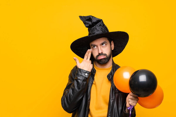 Man with witch hat holding black and orange air balloons for halloween party with problems making suicide gesture