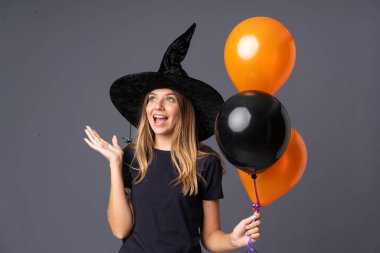 Siyah ve turuncu hava balonlarını tutan genç cadı sürpriz bir yüz ifadesiyle