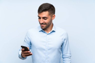 Cep telefonu izole edilmiş mavi duvarlı genç yakışıklı adam çok gülümsüyor.