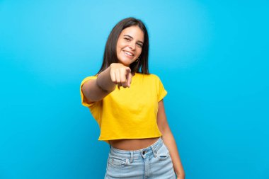İzole edilmiş mavi arka plandaki genç kız kendine güvenen bir ifadeyle seni işaret ediyor.