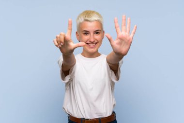 Mavi duvarın üzerinde beyaz kısa saçlı genç kız parmaklarıyla yediyi sayıyor.