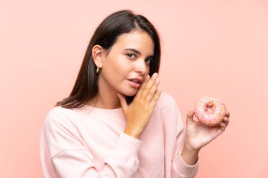 Soyutlanmış pembe arka planda donut tutan genç kız bir şeyler fısıldıyor