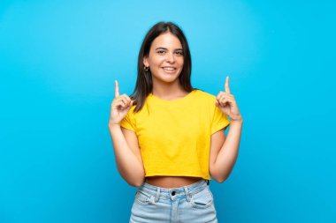 İzole edilmiş mavi arka planı olan genç bir kız harika bir fikre işaret ediyor.